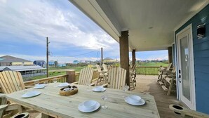 Terraza techada al aire libre con una mesa de comedor dispuesta para cuatro personas, rodeada de sillas de madera, con vistas a un área verde.