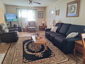A living room with a sofa, armchair, TV, and a patterned rug. - The Thompson House (Tryon)