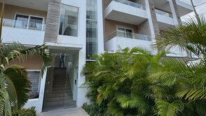 Un edificio de varios pisos con balcones, una escalera central y abundante vegetación.