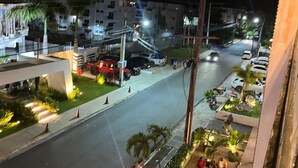 Vista nocturna de una calle con coches estacionados, un paso de peatones y un edificio con balcón que da a la calle.