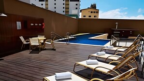 Un espace piscine aménagé sur le toit, avec des chaises longues et une petite table, le tout entouré d’une terrasse en bois.