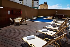 Un espace piscine aménagé sur le toit, avec des chaises longues et une petite table, le tout entouré d’une terrasse en bois.