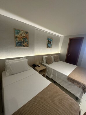 Een hotelkamer met twee enkele bedden, een nachtkastje met telefoon en afstandsbediening, en twee aan de muur hangende schilderijen.