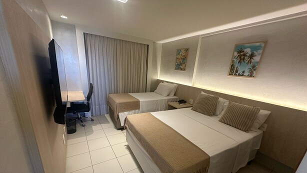 Een hotelkamer met een groot bed, twee kleinere bedden, een bureau met stoel, een televisie en twee schilderijen aan de muur.