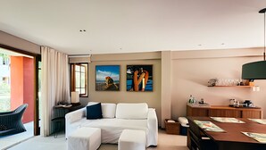 A modern living room with a sofa, ottomans, a dining table, and artwork on the walls. - Village with 2 Suites Facing Timeantube Lagoon - Timeantube Reserve, Praia do Forte (Açu da Torre)