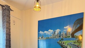 Een woonkamer met een bank, twee kussens, een salontafel en een schilderij van een stadsgezicht.