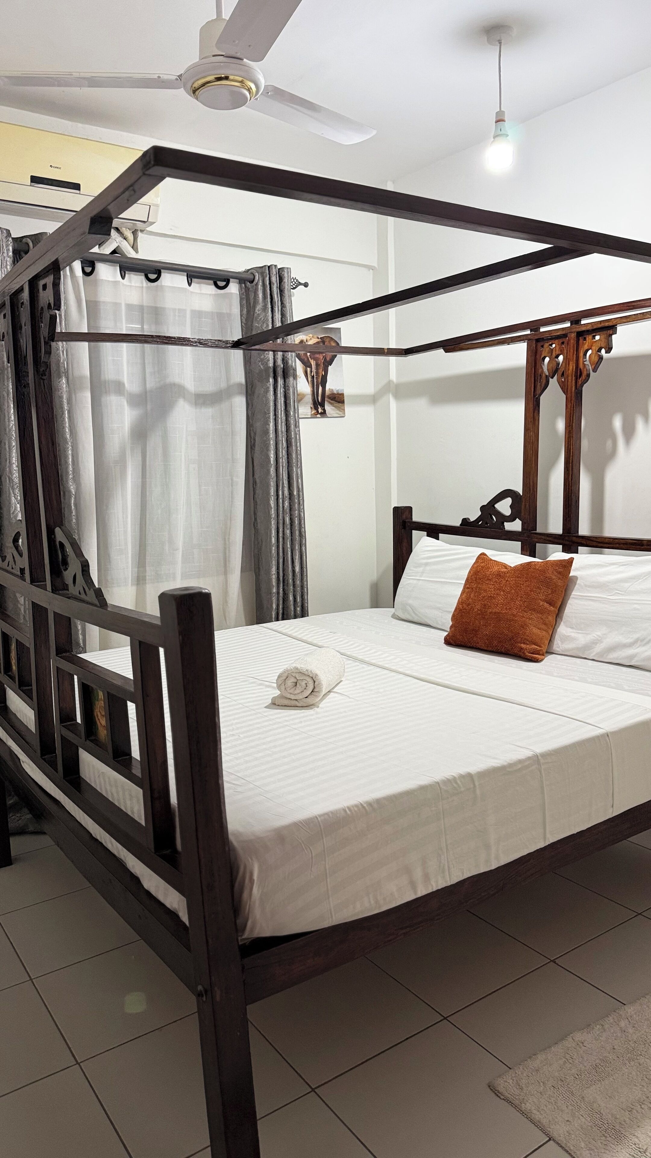 Una cama con dosel, un colchón blanco, una almohada marrón y una toalla blanca enrollada.