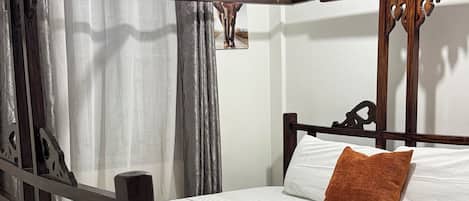 Una cama con dosel, un colchón blanco, una almohada marrón y una toalla blanca enrollada.