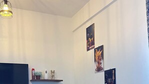 Een woonkamer met een televisie, een eettafel, stoelen, een vloerkleed en wanddecoratie.