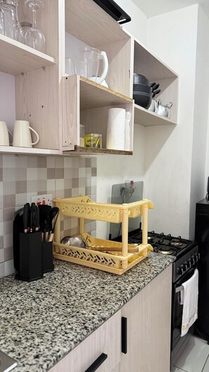 A kitchen with a granite countertop, a yellow cutting board, a stove, and various kitchen utensils. - Buxton 2 bedroom apartment- WITH AC/HOT SHOWER| NETFLIX (Mombasa)