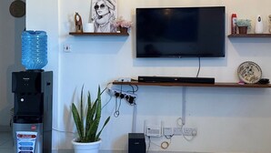 Een moderne woonkamer met een flatscreen televisie, een waterdispenser, een potplant en een decoratieve plafondlamp.