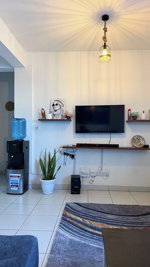 A modern living room with a flat-screen TV, a water dispenser, a potted plant, and a decorative ceiling light. - Buxton 2 bedroom apartment- WITH AC/HOT SHOWER| NETFLIX (Mombasa)