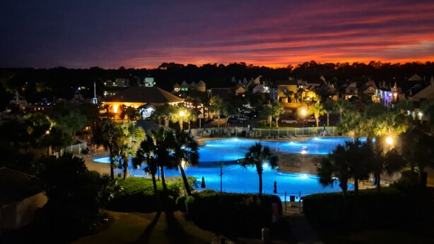 A resort with a large swimming pool, palm trees, and illuminated buildings at dusk. - Waterway View • 2300 sqft 4BR/4BA • Barefoot Golf (North Myrtle Beach)