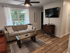 A living room with a sofa, a coffee table, a TV, and a wooden floor. - The Hammer Cottage (Inverhuron)