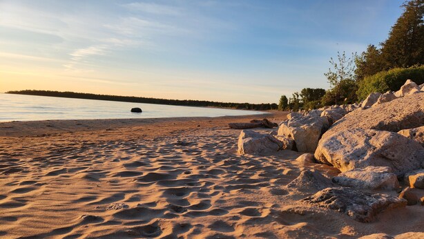 Ein sandiger Strand mit großen Felsen und ruhigem Wasser.