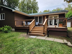 A wooden house with a deck, a staircase, and a front door. - The Hammer Cottage (Inverhuron)