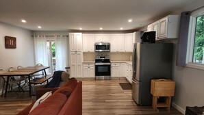 Eine moderne Küche mit weißen Schränken, Edelstahlgeräten, einem Holztisch und einem roten Sofa.