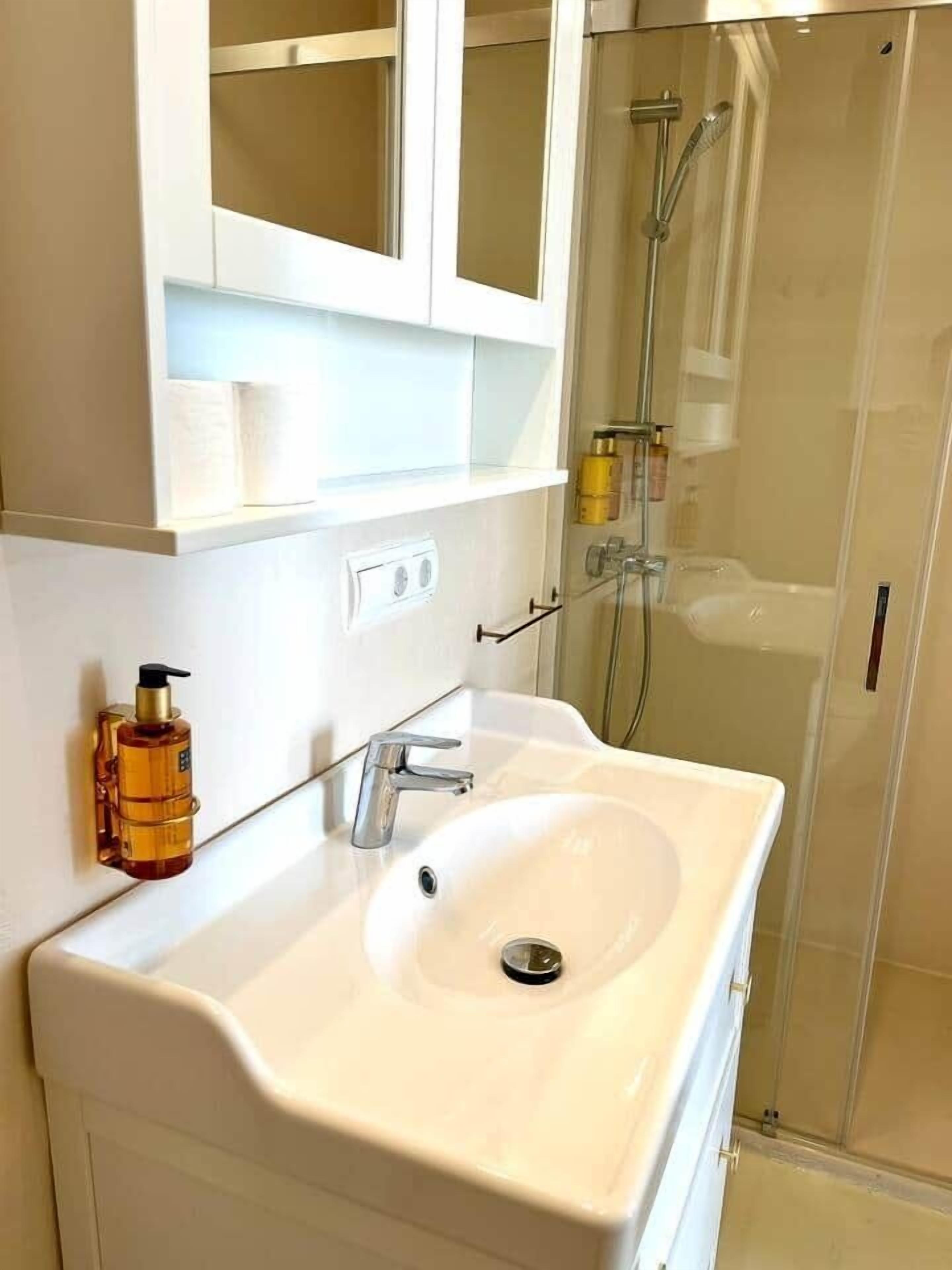 Een badkamer met een witte wastafel, een spiegel en een douchecabine.
