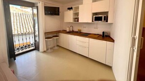 Een kleine keuken met witte kastjes, een magnetron en een houten aanrecht.
