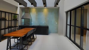A modern kitchen with a wooden table and chairs, a large stove, and a view through a glass door. - Studio SC (São Paulo)