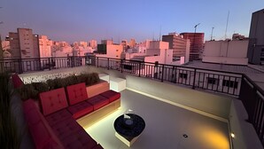 A rooftop terrace with a red sofa, a small table, and a decorative plant. - Studio SC (São Paulo)