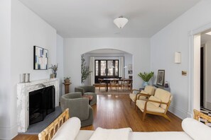 A living room with a fireplace, seating area, dining table, and a view through a large window.