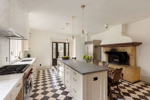 Une cuisine avec un carrelage à motifs, un îlot central, un four encastré et des luminaires suspendus.
