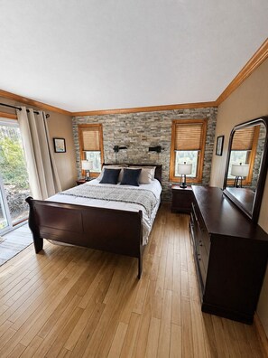 Un dormitorio con pared de piedra, suelo de madera, una cama, mesitas de noche y un aparador.