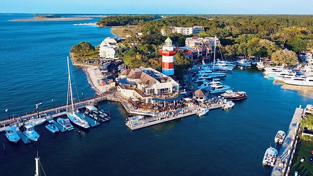 Un port de plaisance situé sur la côte, avec des bateaux amarrés, un phare et un bâtiment doté d’un balcon donnant sur l’eau.