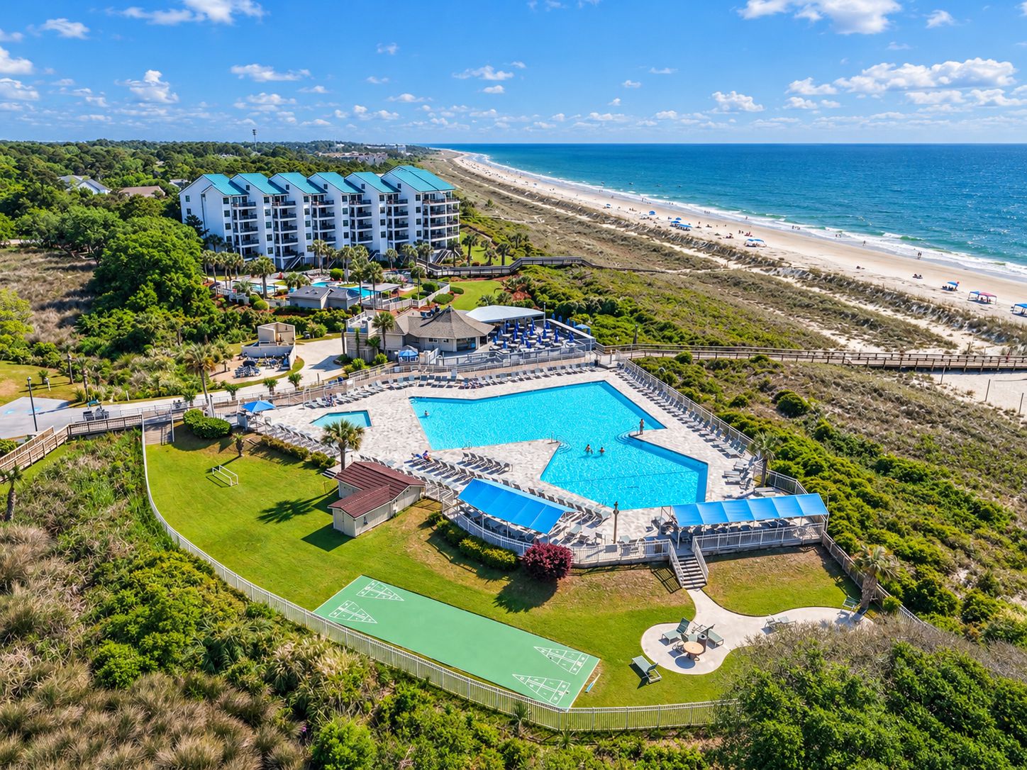 A resort with a large swimming pool, tennis courts, and a beach view.
