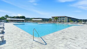 Une piscine avec une terrasse carrelée, des chaises longues et un bâtiment en arrière-plan.