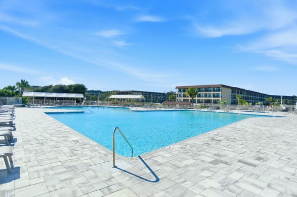 A swimming pool with a tiled deck, lounge chairs, and a building in the background.