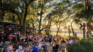 Un espace de restauration en plein air, avec des tables et des chaises, entouré d’arbres et offrant une vue sur un plan d’eau.