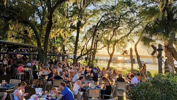 An outdoor dining area with tables and chairs, surrounded by trees and overlooking a body of water.