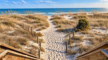 A sandy beach path leading to wooden structures, with the ocean in the background.