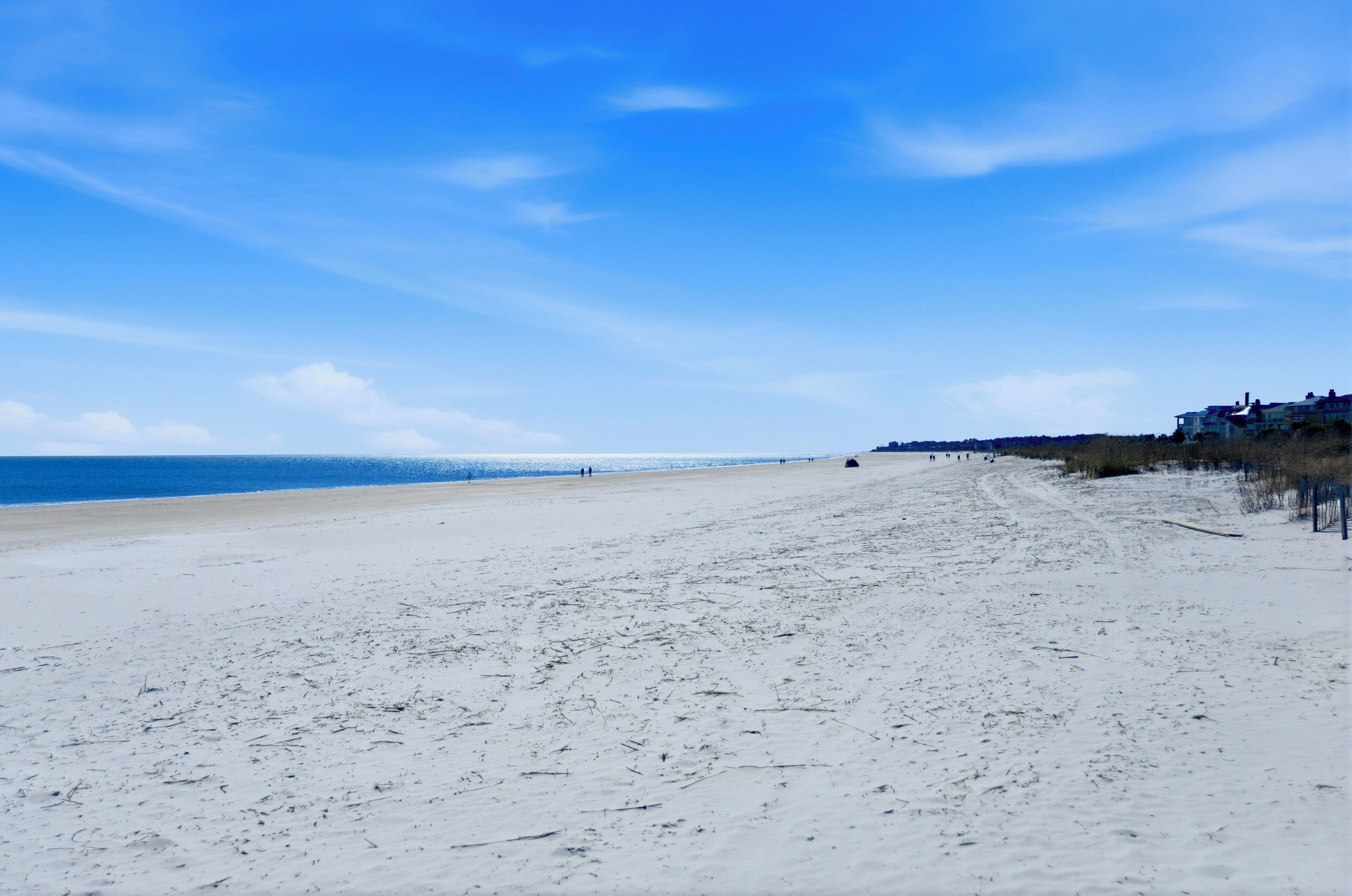 A beach with a clear sky, sandy shore, and buildings in the distance.
