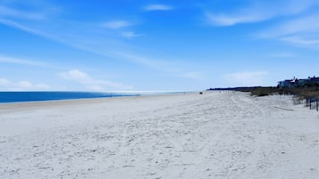 A beach with a clear sky, sandy shore, and buildings in the distance.