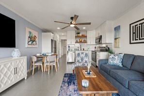 Une cuisine moderne avec des meubles blancs, un coin repas avec une table et des chaises en bois, et un salon avec un canapé et une table basse.