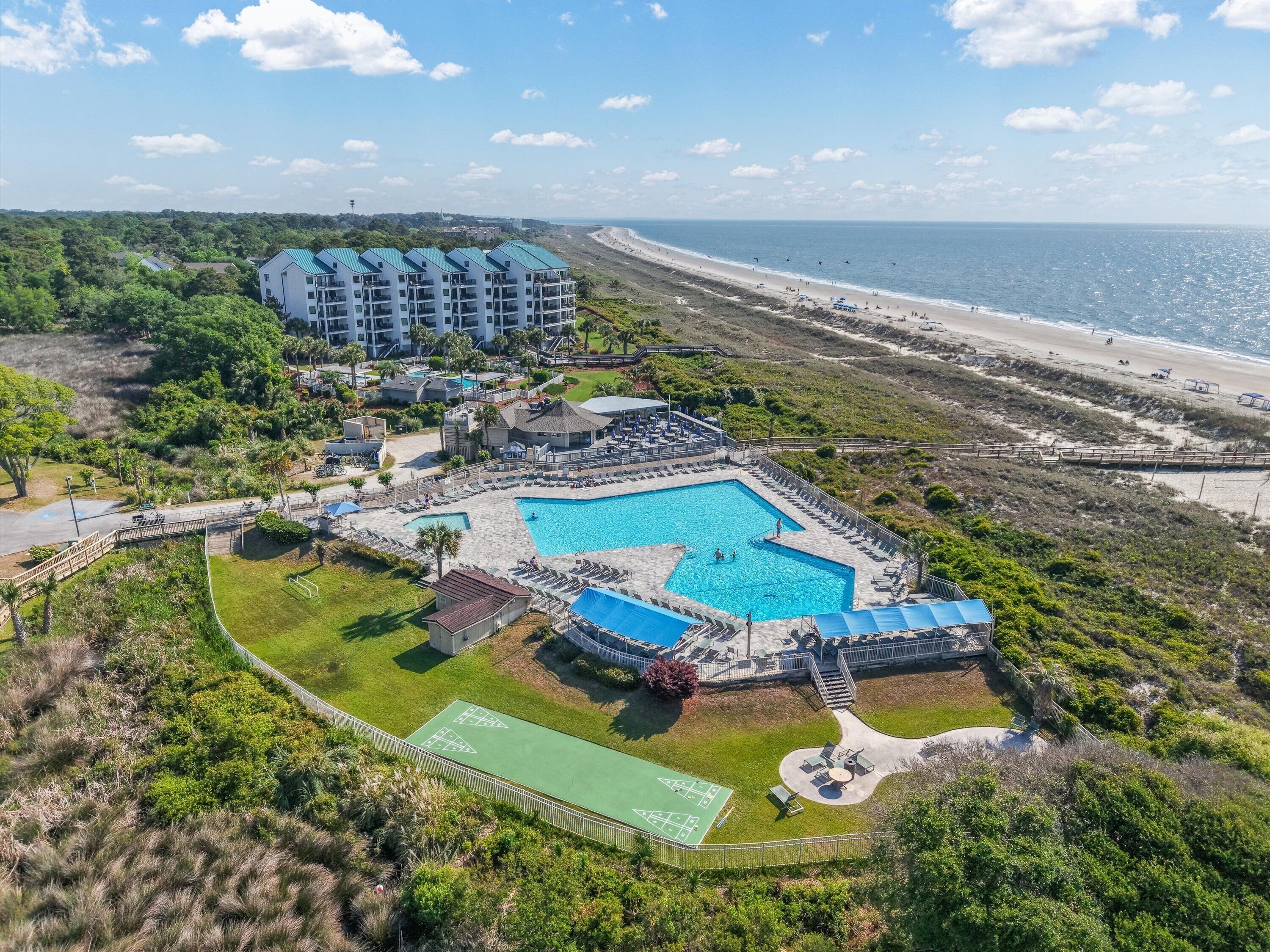 A resort with a swimming pool, tennis courts, and a beach view.