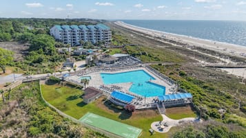 A resort with a swimming pool, tennis courts, and a beach view.