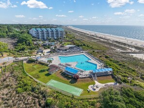 Een resort met een zwembad, tennisbanen en uitzicht op het strand.
