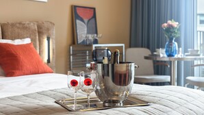 A hotel room with a bed, a bedside table with a vase, a framed artwork, and a window with curtains. - LILY APART Żurawie Premium stay (Gdańsk)