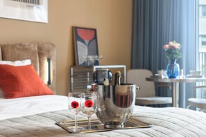 Ein Hotelzimmer mit Bett, Nachttisch mit Vase, gerahmtem Kunstwerk und einem Fenster mit Vorhängen.