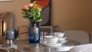 A round metal table with a blue vase of flowers, white bowls, and a glass. - LILY APART Żurawie Premium stay (Gdańsk)