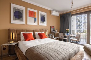A hotel room with a large bed, a small table, a chair, and a balcony with a view of buildings. - LILY APART Żurawie Premium stay (Gdańsk)