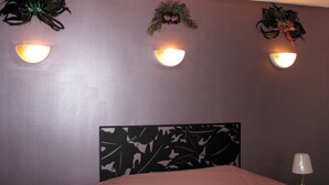 Une chambre avec un lit, deux lampes fixées au mur et une tête de lit décorative.