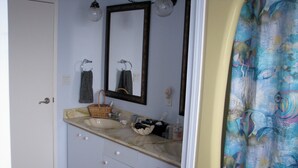 Une salle de bain avec un double lavabo, un miroir, un porte-serviettes, un panier et un rideau de douche.