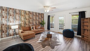 A living room with a brown leather sofa, a glass coffee table, a wooden bookshelf, a cowhide rug, and a wooden wall with a vertical pattern. - Private Pool & Patio & Poker & Kids Play Room (San Antonio)