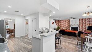 A modern kitchen with a central island, a dining area with a table and chairs, and a living room with a sofa and fireplace. - Private Pool & Patio & Poker & Kids Play Room (San Antonio)