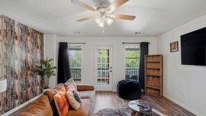 A living room with a brown leather sofa, a ceiling fan, a glass coffee table, and a wooden bookshelf. - Private Pool & Patio & Poker & Kids Play Room (San Antonio)